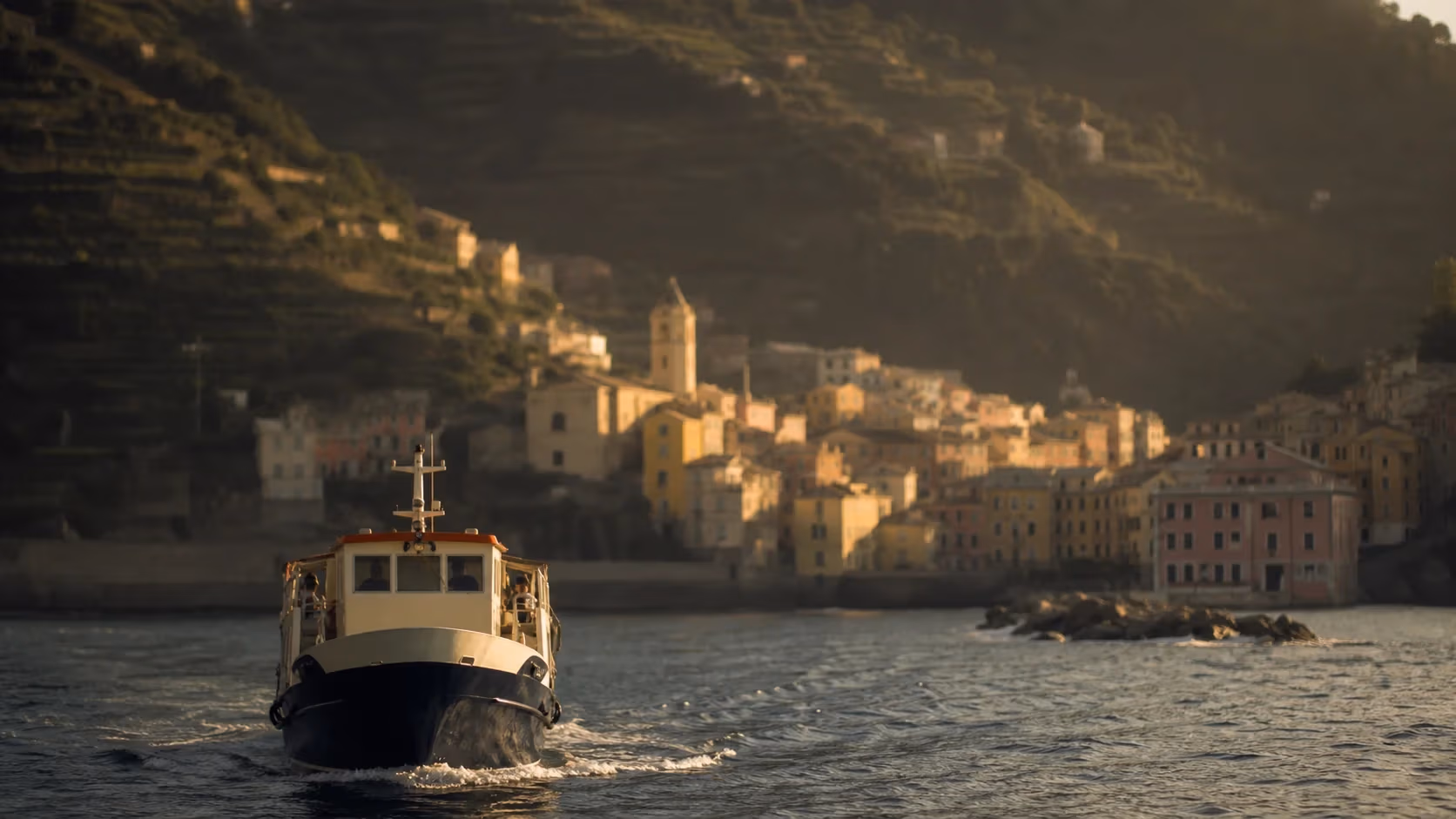 "Battello che si avvicina a un borgo delle Cinque Terre dal mare nel tardo pomeriggio"