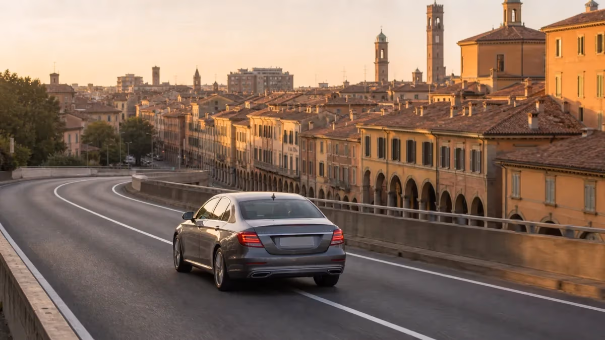 "Auto con autista verso il centro di Bologna con i portici e i tetti rossi sullo sfondo"